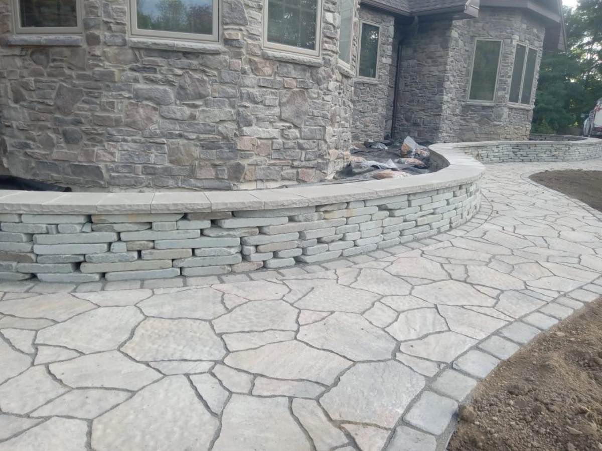 A wide natural stone patio behind a large stone home