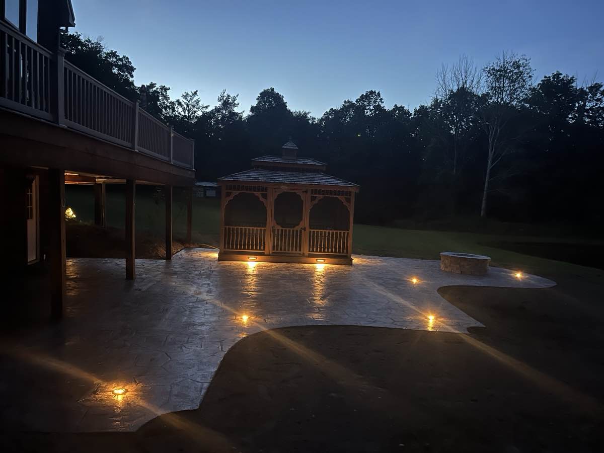 A gazebo and stone fire pit on a patio at twilight